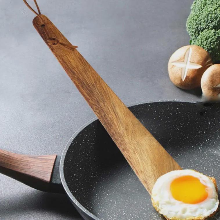 Wooden spatula on a frying pan with an egg and vegetables on a gray background